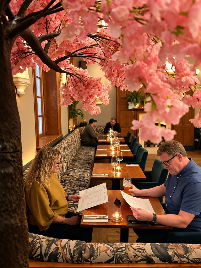 Guests at their tables beneath the pink blossom tree, with green banquettes and candles lit.