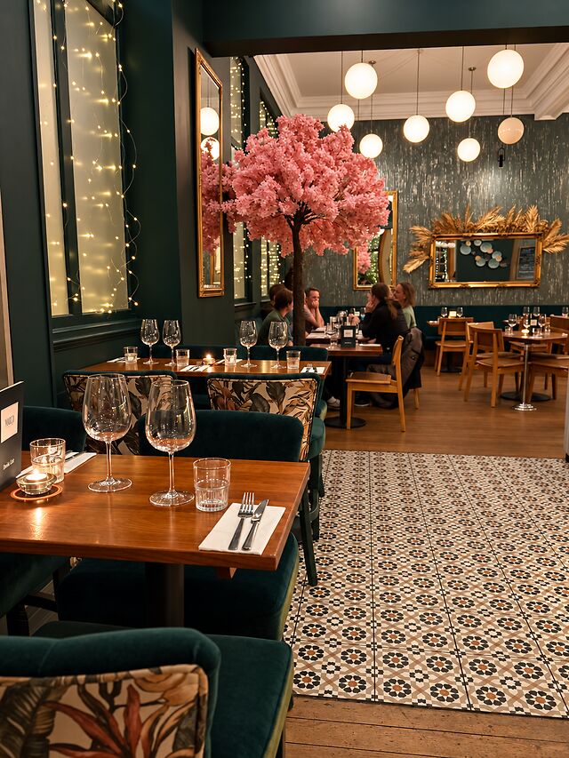 The Miro Greek dining room, with pink blossom, globe lights, patterned floor tiles and green banquettes.