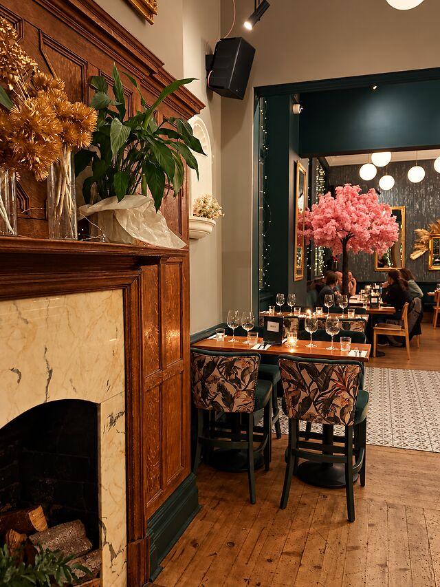 A carved timber fireplace in the dining room, with the blossom tree and globe lights beyond.