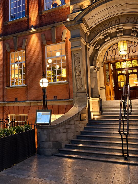 The stone archway of the Treasury Building at dusk, with warm windows and a lit street lamp.