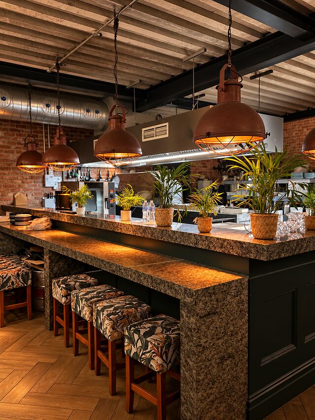 The kitchen pass, with a granite counter, patterned bar stools and copper pendant lamps.
