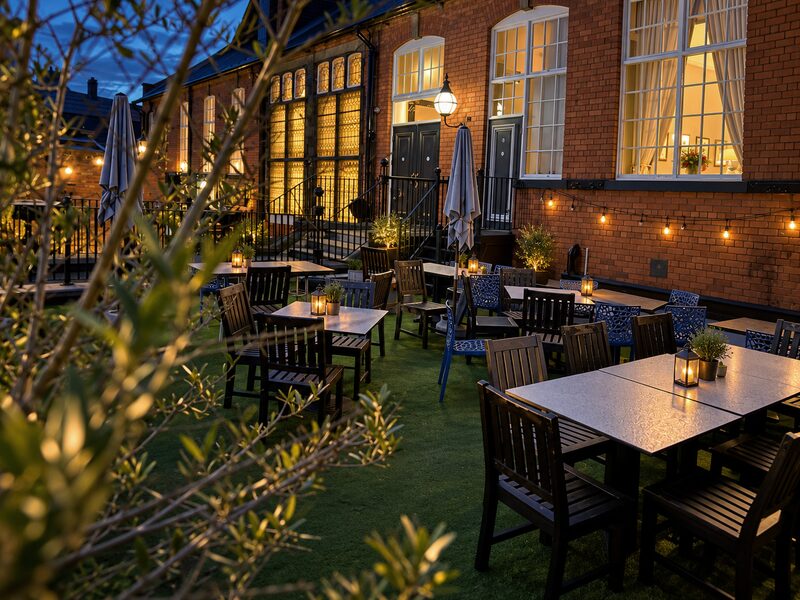 An olive branch in the foreground, with lanterns and the lit windows of the terrace behind.