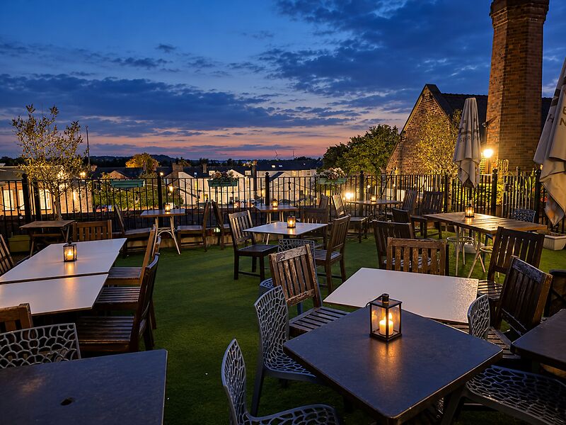 The rooftop terrace at sunset, with lanterns on the tables and a pink and blue sky over the rooftops.