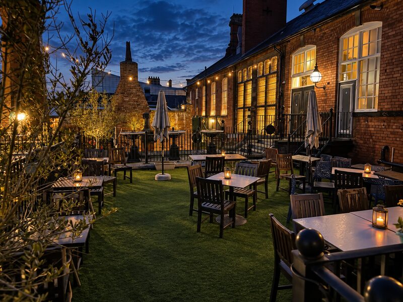 The terrace at dusk, with lanterns on the tables and warm light along the red-brick building.